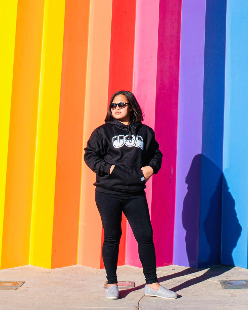 HHand printed USA Hoodie Black on female model in front of colorful background.