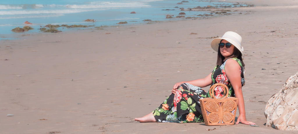 Woman on beach wearing summer dress with rattan butterfly tote, both handmade in Bali, Indonesia.