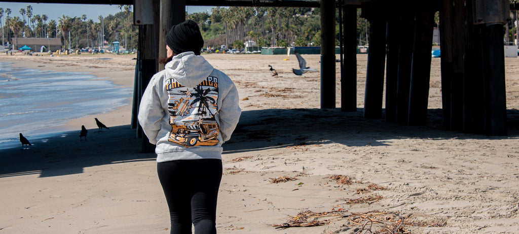 Woman walking on the beach wearing hand-printed gray hoodie showing image of iconic Philippines jeepney bus.