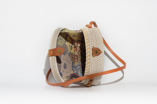 Round white rattan bag handwoven In Bali Indonesia, featuring painted wooden inlay of girl holding sunflowers, with leather strap & brass clasp, showing colorful cotton lining.