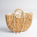 Roomy tote bag handmade in Bali from water hyacinth leaves, pictured to show sturdy overlapping weave with flat bottom and rounded sides. Sturdy round handles are woven directly into body. Light tan in color. Displayed to show white cotton lining pulled up & cinched closed with drawstring.