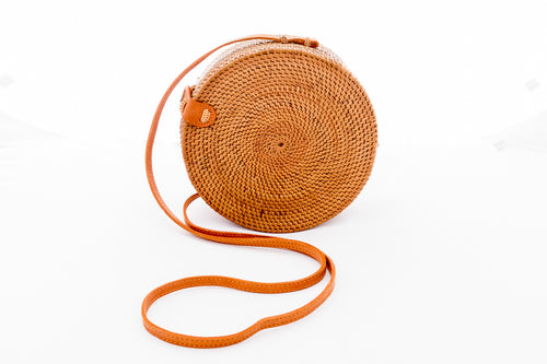 Natural rattan round handbag hand woven in Bali Indonesia, showing tight rattan weaving in a simple spiral pattern, leather strap & brass clasp.