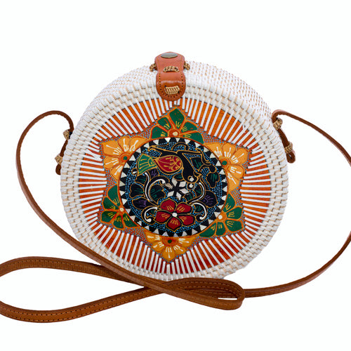 Round white rattan bag hand woven in Bali with hand painted insert featuring a bird & flowers in many colors, inside a yellow & green star, with a leather strap & brass clasp.