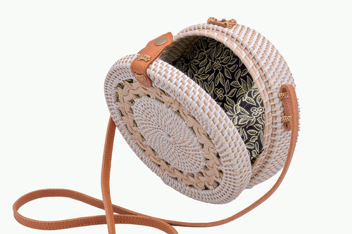 White rattan handbag hand woven in Bali Indonesia, with braided design, leather strap & brass clasp, showing detail of colorful, patterned lining.