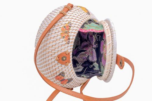 White rattan handbag hand woven in Bali Indonesia with butterfly decals, leather strap & brass clasp, showing colorful, patterned cotton lining.