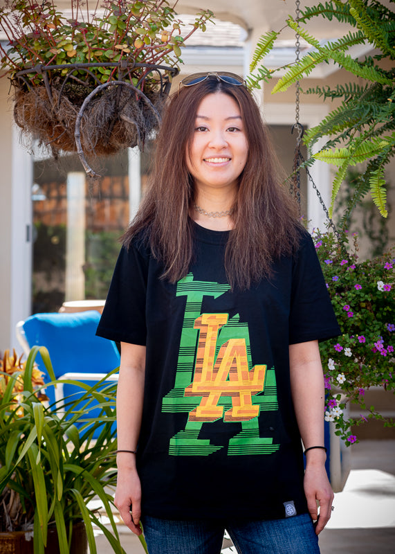 Black T-shirt, front side, hand printed with a double image of the text "LA" in yellow, orange & green, pictured on female model.