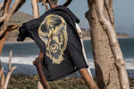 Black T-shirt front side showing face of American Buffalo hand printed in gold & yellow colors, pictured on driftwood.